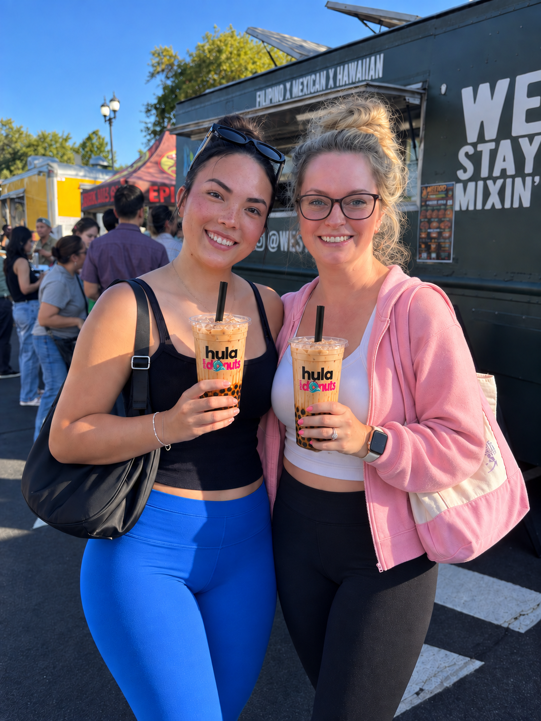 Two smiling friends holding Hula Mini Donuts boba milk teas at an outdoor food truck event